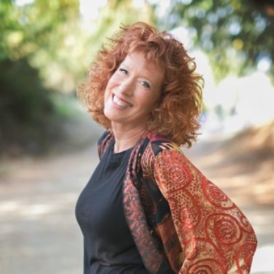 Portrait of Spiritual New Though musician Karen Drucker. image of her posing outside wearing a red shall. image features a woman with red hair smiling