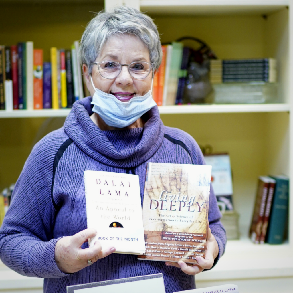 Image of older woman wearing a purple sweater holding new thought books at Center for Spiritual Living Chico s in house Bookstore social distancing bookstore