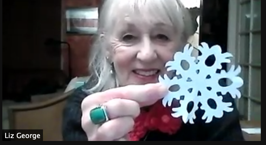 photo of online event of woman making cut outs of paper snow flakes in a zoom event for Christmas