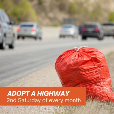 image of trash being picked up in an orange trash bag by a busy highway